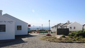 Een gebouw aan de kust met een bord waarop staat 'Ontmoet de kunstenaars!' en een bank op de voorgrond.
