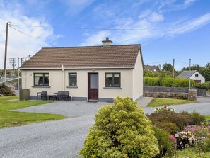 Een gelijkvloers huis met een pannendak, een voordeur en een klein terras met buitenmeubels.