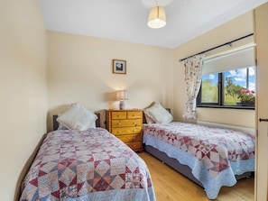 A bedroom with two single beds, a dresser, a lamp, a framed picture on the wall, and a window with a view of greenery. - Spiddal Cottage (Spiddal)