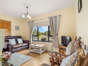 Een woonkamer met een leren bank, een houten salontafel, een tv op een houten dressoir, en een raam met gordijnen.