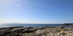 Une côte rocheuse, sous un ciel dégagé, avec des montagnes qui se dessinent à l'horizon.