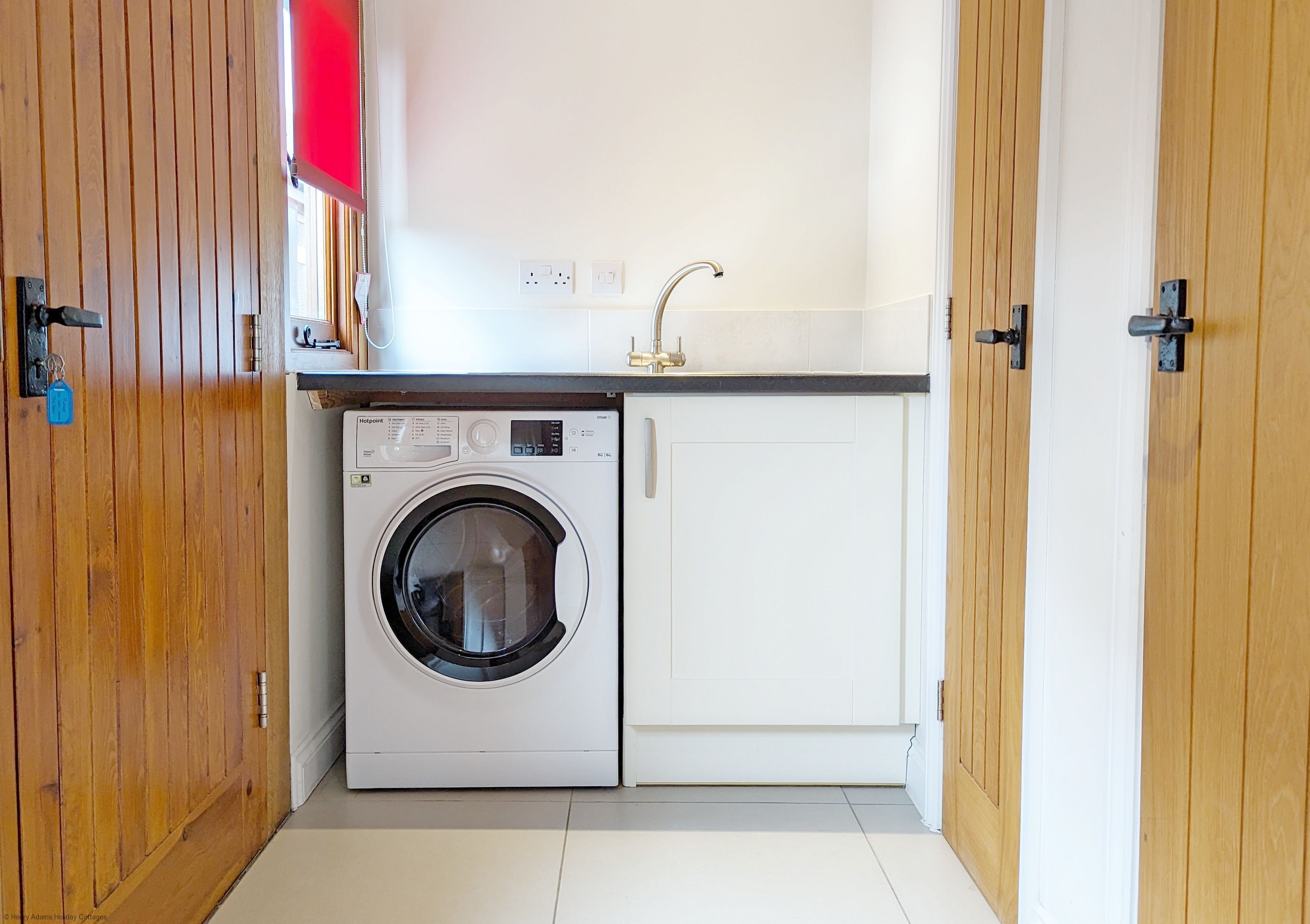 A compact laundry room with a front-loading washing machine, a sink, and wooden doors.