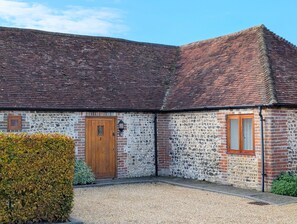 Un bâtiment traditionnel en briques, doté d’une porte en bois et d’une petite fenêtre, entouré de gravier et d’une haie.