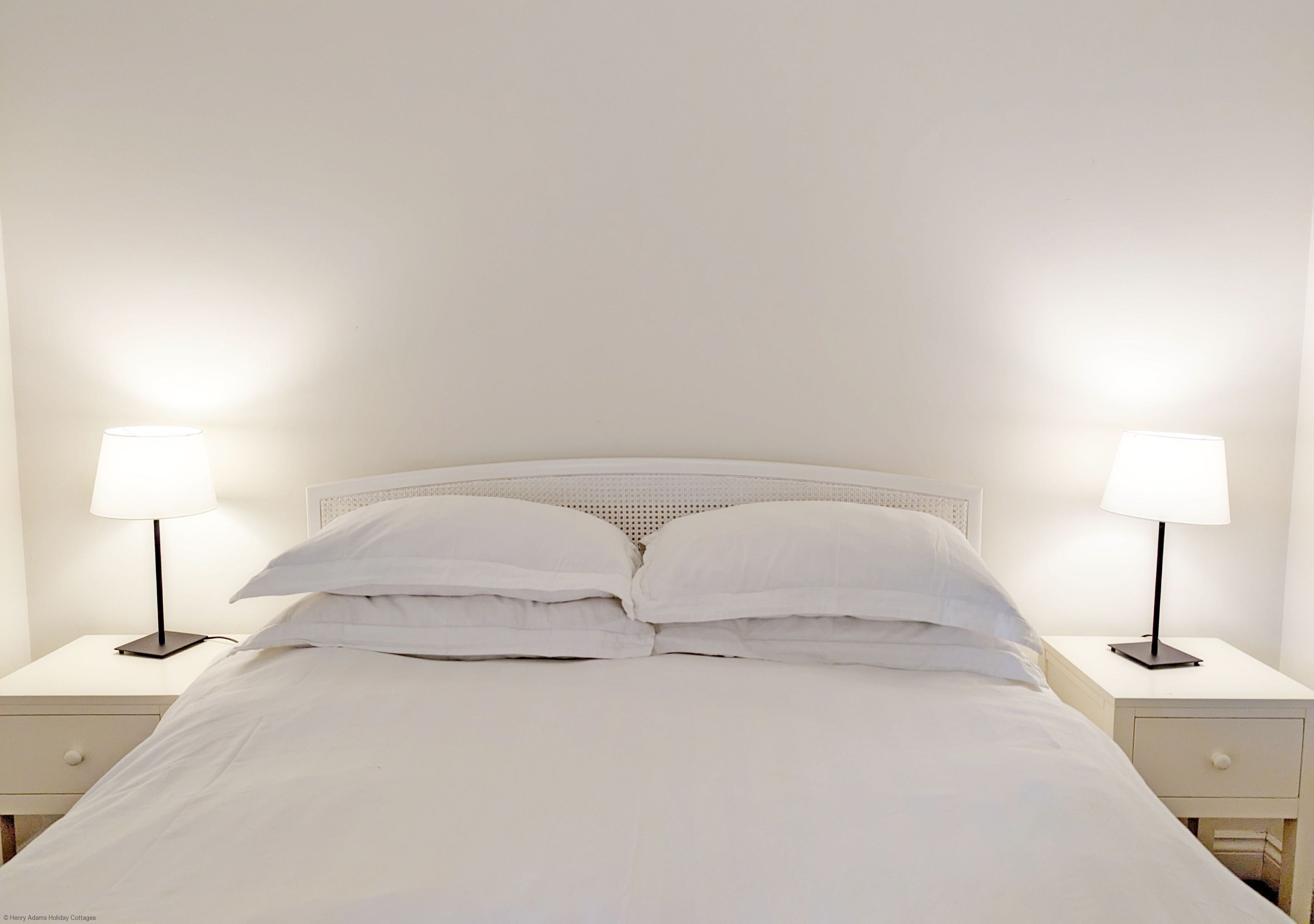 Ein ordentlich bezogenes Bett mit weißen Leinen und je einer Nachttischlampe auf jeder Seite.