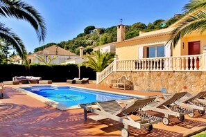 Un espace piscine avec des chaises longues, un mur en pierre et un escalier menant à un bâtiment.