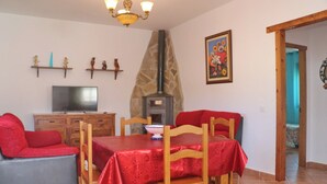 Un coin repas avec une nappe rouge, des chaises en bois, un téléviseur et une cheminée en pierre.