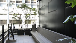 An outdoor seating area with benches and potted plants, adjacent to a modern building with large windows and a dark facade.