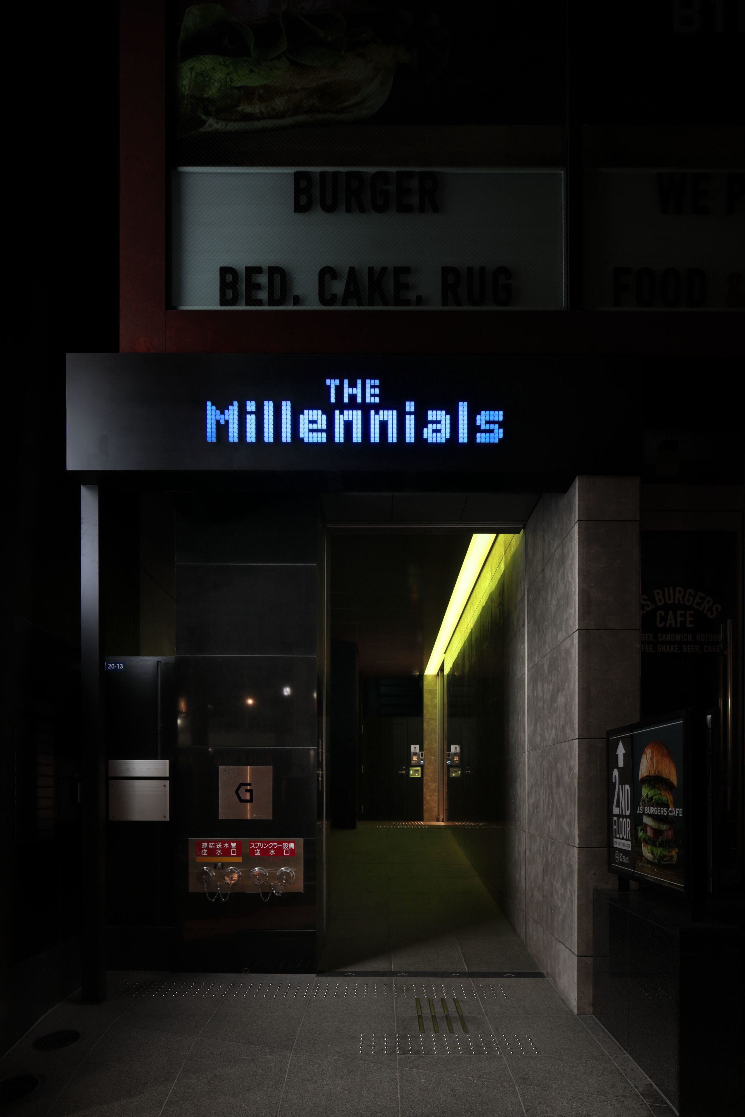 A building entrance with a neon sign reading "THE MILLENNIALS" and a sign above stating "BURGER BED CAKE RUG FOOD".