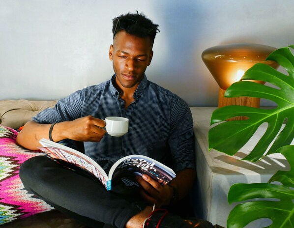 Une personne assise sur un canapé, avec un livre et une tasse à portée de main, une lampe et une plante au premier plan.