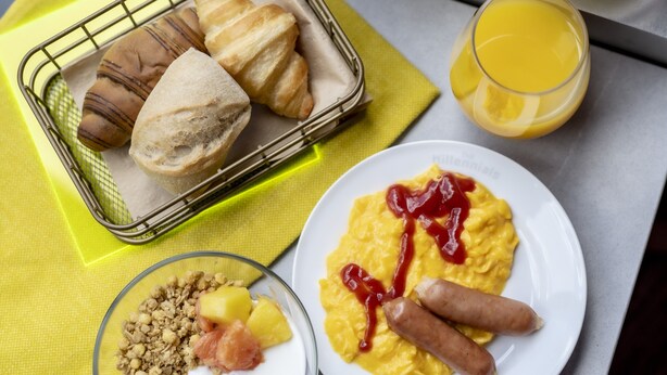 A breakfast tray with croissants, a plate of scrambled eggs with sausage and ketchup, a glass of orange juice, and a bowl of cereal with fruit and granola. - The Millennials Shibuya (Tokyo)