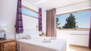 A bedroom with a bed, a nightstand, a lamp, and a view of trees through the window.