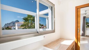 A modern bathroom with a large window, a bathtub, and a view of a mountain and palm trees.
