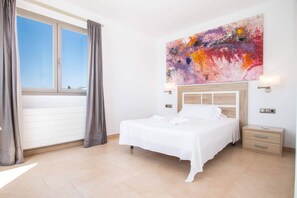Une chambre d’hôtel avec un lit, une fenêtre avec des rideaux, un tableau au mur et une table de chevet.