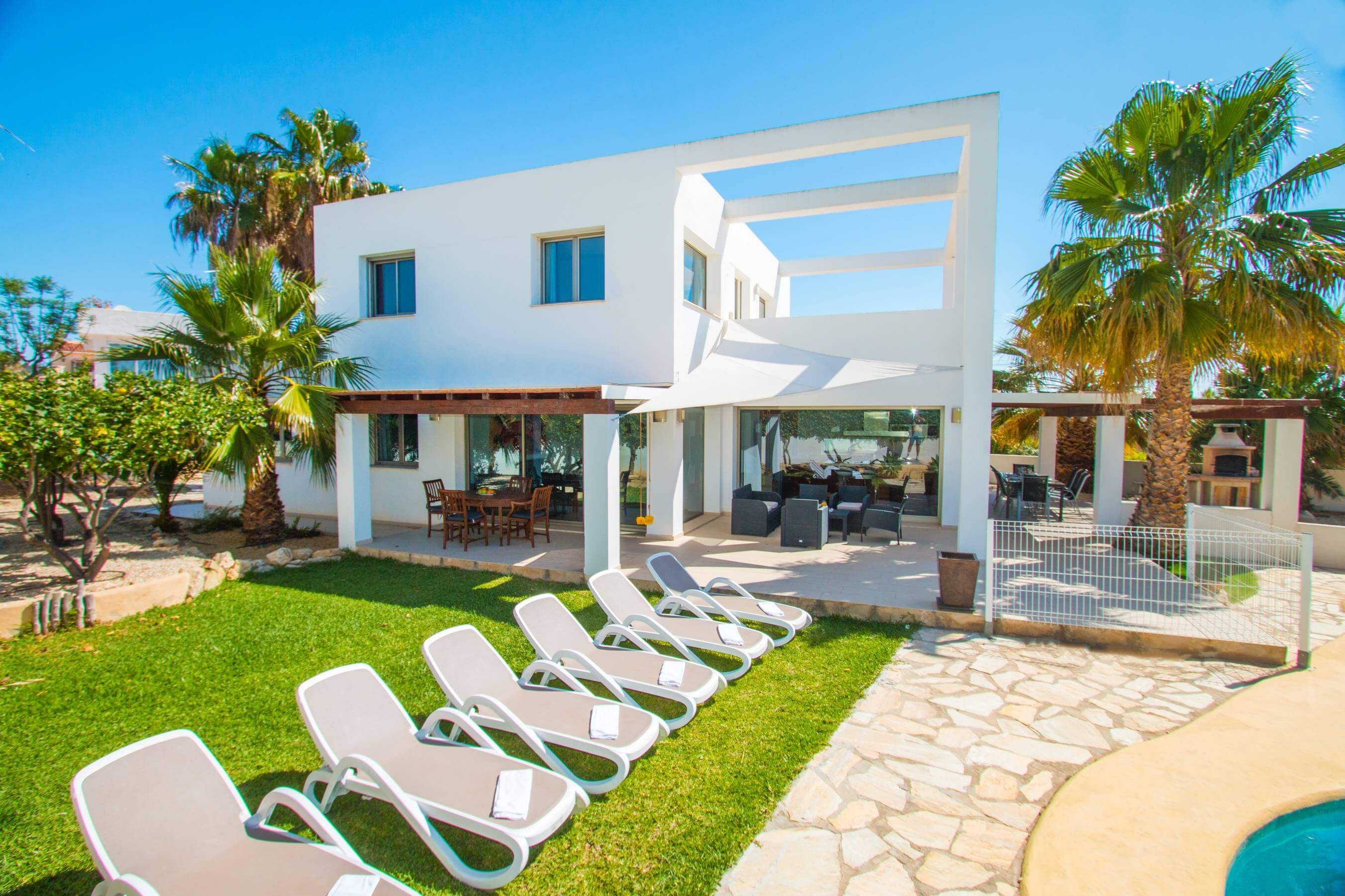 Une maison moderne à deux étages dotée d’un patio, d’un espace salon extérieur et d’une piscine.