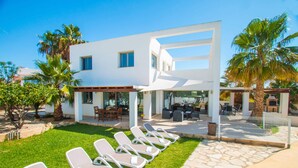 A modern two-story house with a patio area, outdoor seating, and a pool.