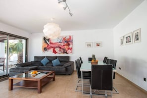 A modern living room with a sofa, coffee table, and dining area with chairs. - Villa Athos - PlusHolidays (Calpe)