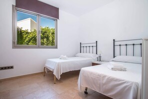 A hotel room with two single beds, a window with a view of greenery, and a white color scheme.