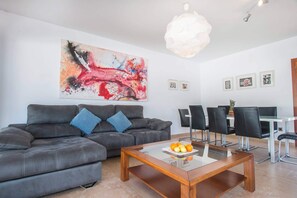 A modern living room with a grey sofa, a coffee table with fruit, and a dining area with chairs and a table.