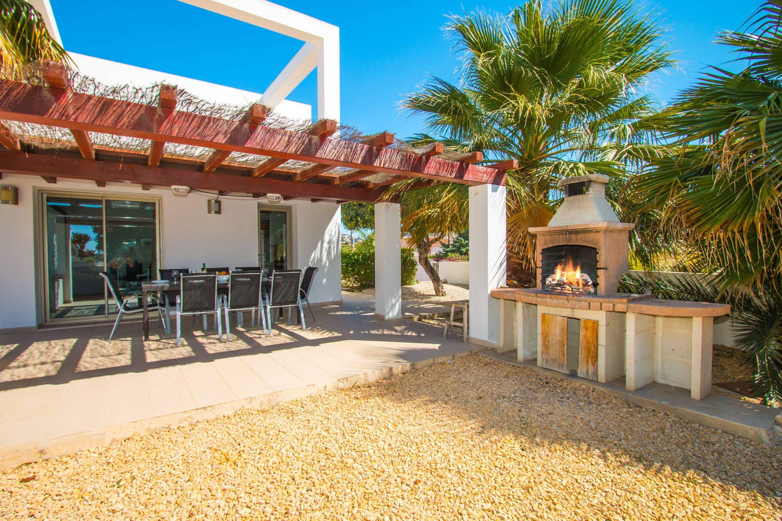 An outdoor patio with a stone fire pit, a pergola, and a dining area with chairs and tables.