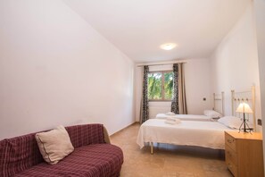Une chambre avec deux lits, un canapé, une table de chevet avec une lampe et une fenêtre avec des rideaux.