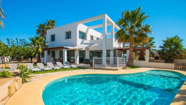 A modern two-story house with a swimming pool, surrounded by palm trees and lounge chairs.