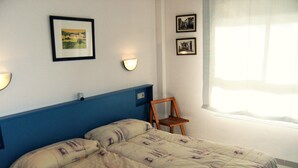 Un dormitorio con una cama, dos luces fijadas a la pared y dos cuadros enmarcados.