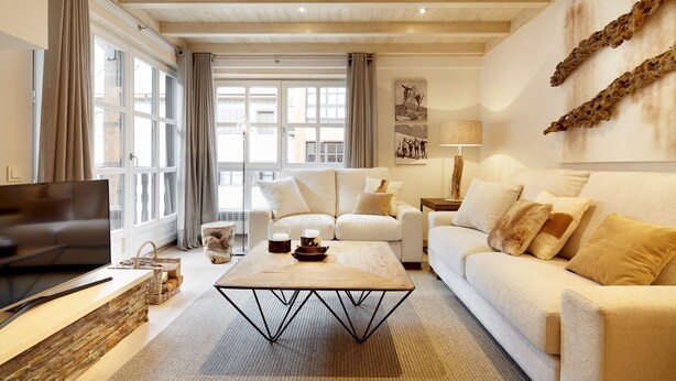 Ett modernt vardagsrum med en stor TV med platt skärm, ett soffbord i trä och en beige soffa.
