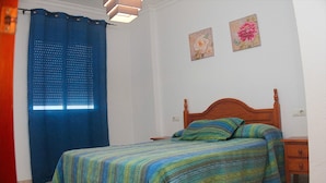 A bedroom with a bed, a nightstand, a wall-mounted lamp, a window with a blue curtain, and two wall art pieces.