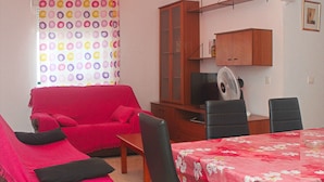 A living room with a red sofa, a wooden cabinet, a TV, and a fan.