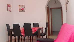 A dining area with a table and chairs, a pink sofa, and a door leading to another room.