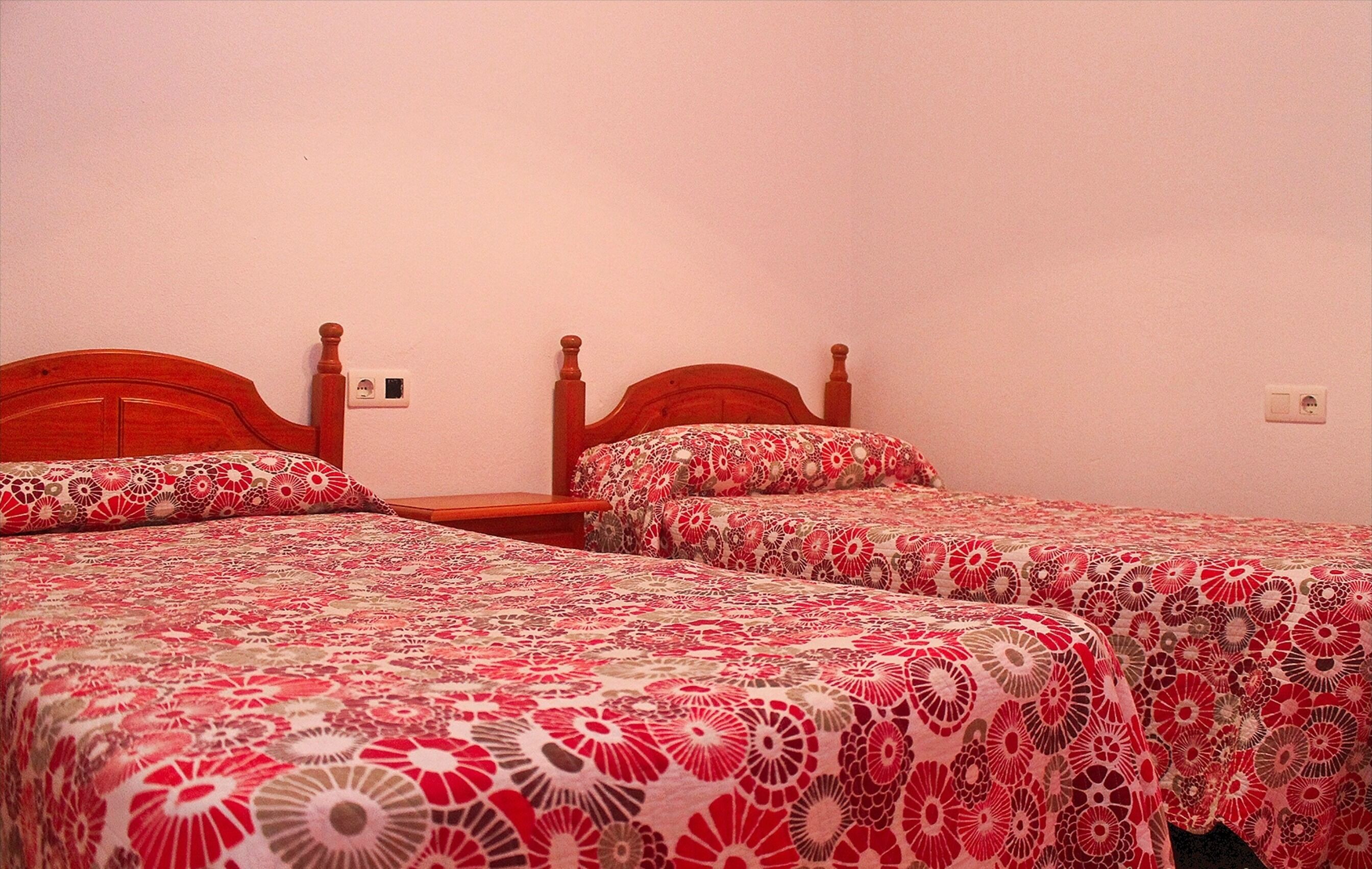 Ein Zimmer mit zwei Holzbettgestellen, jeweils mit blumigem Bettbezug.