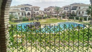 Blick auf ein Schwimmbecken mit umliegendem Garten und einer Reihe von Villen.