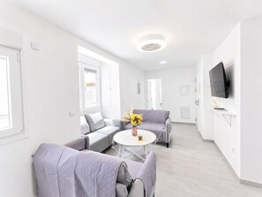 A modern living room with a sofa, armchairs, a coffee table, and a TV mounted on the wall.