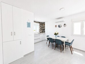 Una cocina moderna con armarios blancos, un comedor con mesa y sillas, y un ventanal con vistas.