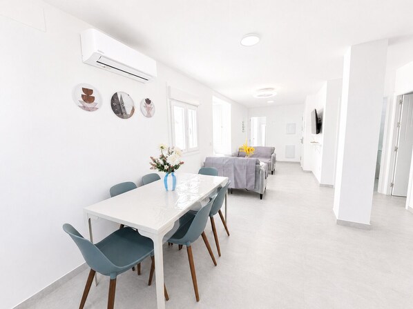 A modern, white interior with a dining area, a sofa, and a TV.