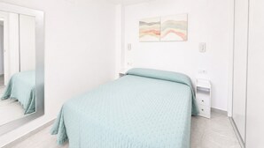 A bedroom with a bed, a bedside table, a mirror, and a wall-mounted artwork.