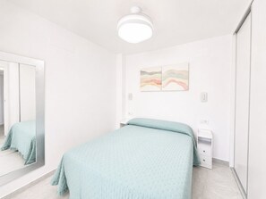 A bedroom with a bed, a bedside table, a mirror, and a wall-mounted artwork.