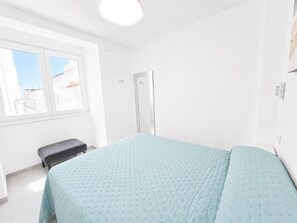 A bedroom with a bed, a bench, a door, and a window.