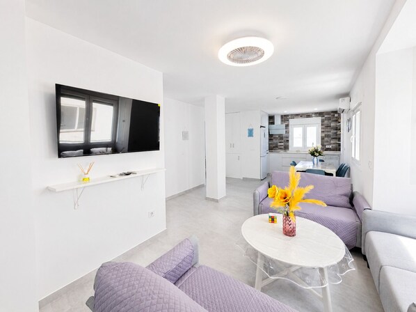 A modern living room with a flat-screen TV, a round table, and a sofa. - 3 bedroom apartment with WiFi near beach (Conil de la Frontera)