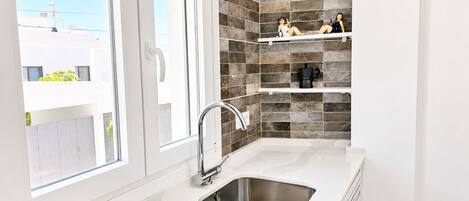 A modern kitchen with a large window, a stainless steel sink, and decorative shelves.