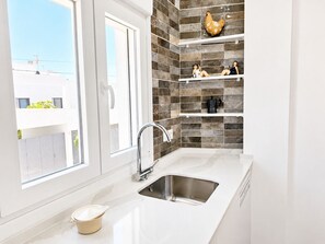 A modern kitchen with a large window, a stainless steel sink, and decorative shelves.