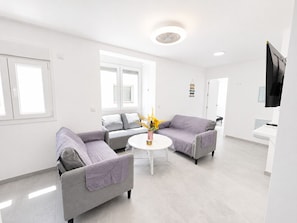 A modern living room with two grey sofas, a white coffee table, and a TV mounted on the wall.