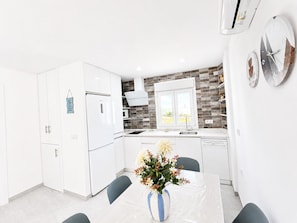 A modern kitchen with white cabinets, a refrigerator, a microwave, and a sink. There is a dining table with chairs and a vase of flowers.