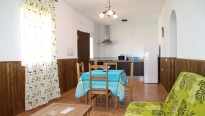 Een eetgedeelte met een houten tafel en stoelen, een bank en een keuken op de achtergrond.