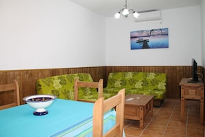 A dining area with a wooden table, chairs, a green sofa, and a painting on the wall.