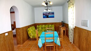 Een eetgedeelte met een tafel gedekt voor twee personen, een houten bank en een schilderij aan de muur.