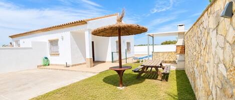 A patio area with a thatched umbrella, a stone wall, and a pool.