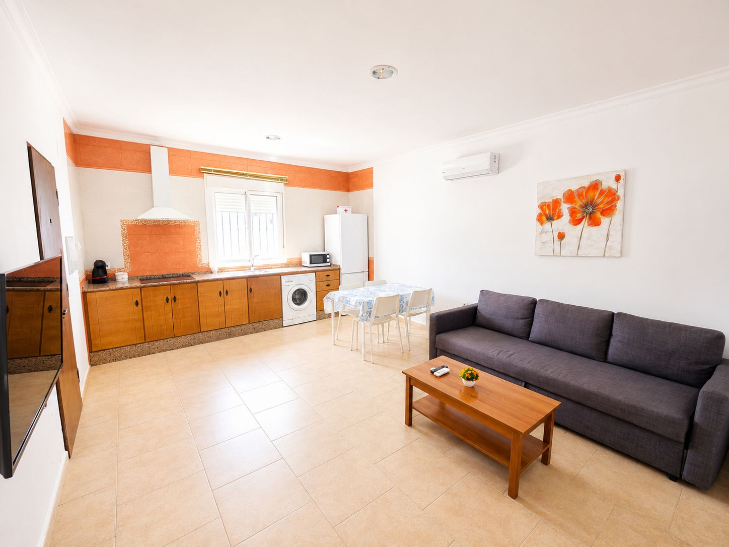 Un espacio habitable compacto con kitchenette, comedor y zona de estar con sofá y mesa de centro.