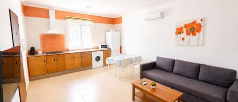 Un espacio habitable compacto con kitchenette, comedor y zona de estar con sofá y mesa de centro.