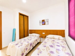 A bedroom with two beds, a wooden wardrobe, a small bedside table, and a wall-mounted artwork. - Chalet Playa Roche . (Conil de la Frontera)